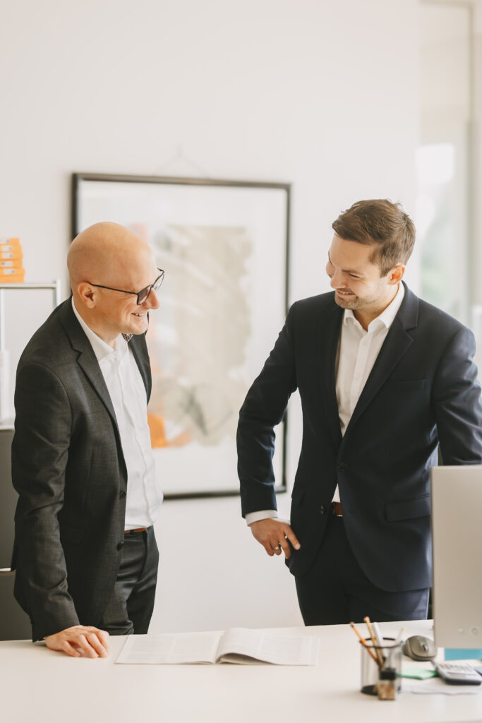 Zwei Mitarbeiter unterhalten sich an einem Schreibtisch und lächeln