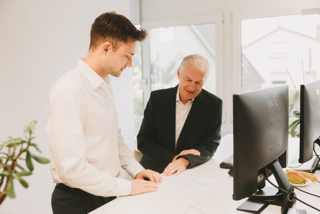 Ein junger Mann und ein älterer Mann besprechen etwas vor Computern